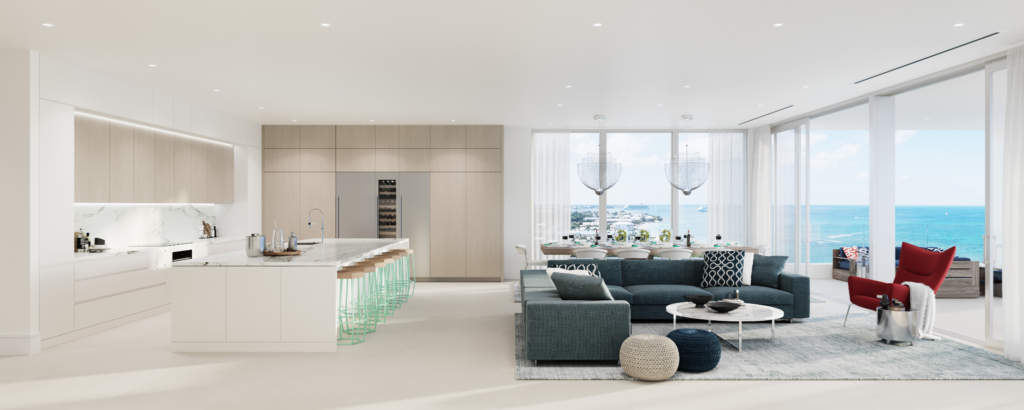 An open-concept luxury penthouse interior featuring a minimalist marble kitchen island, a spacious blue sectional sofa living area, and floor-to-ceiling glass doors opening to panoramic Caribbean ocean views.