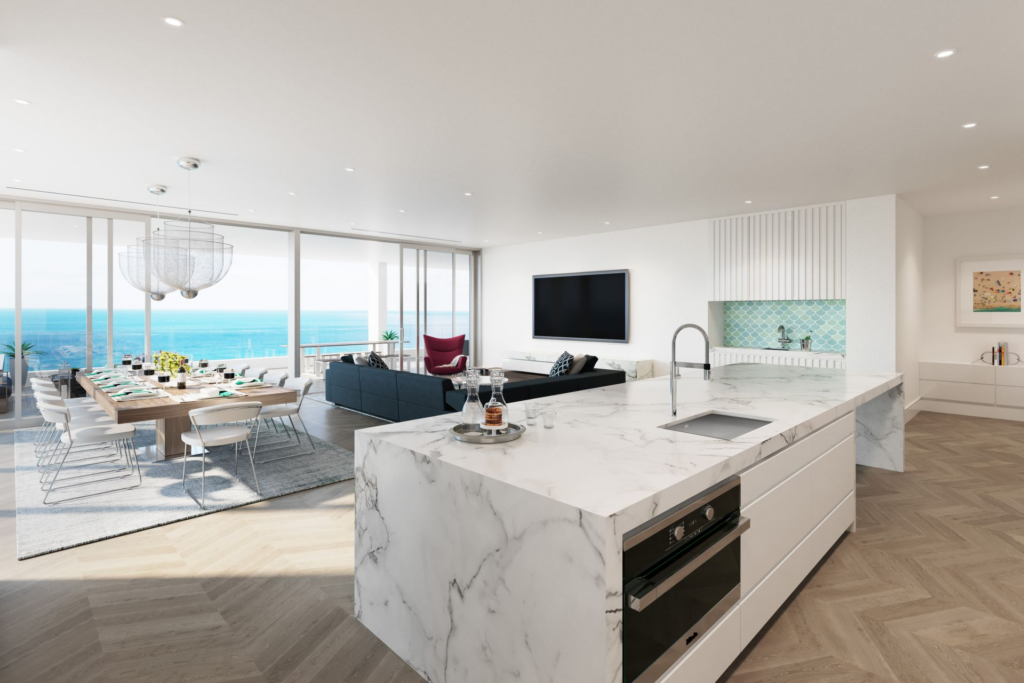 A luxury open-plan beachfront residence interior featuring a large white marble waterfall kitchen island, a modern dining area, and floor-to-ceiling glass walls showing pristine Caribbean ocean views.