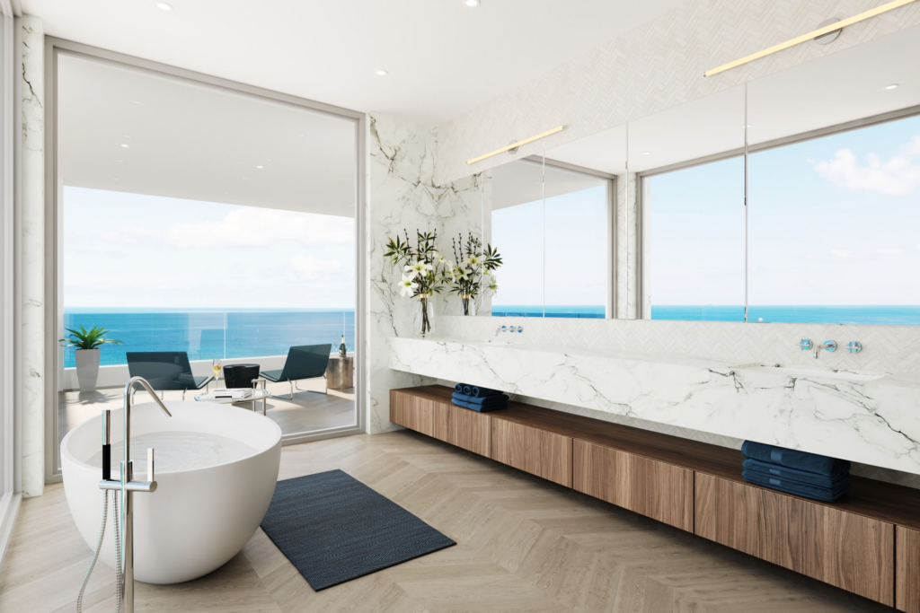 A luxury primary bathroom featuring a freestanding soaking tub, a long marble floating vanity, and floor-to-ceiling glass doors opening onto an oceanfront terrace.