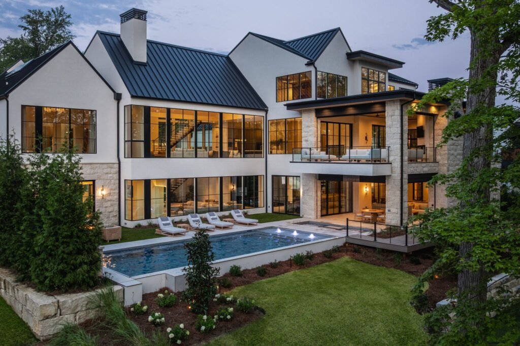 Exterior architectural view of "The Reverie" luxury estate in Zionsville, Indiana, showcasing the multi-level modern design, custom pool, and illuminated floor-to-ceiling windows at dusk