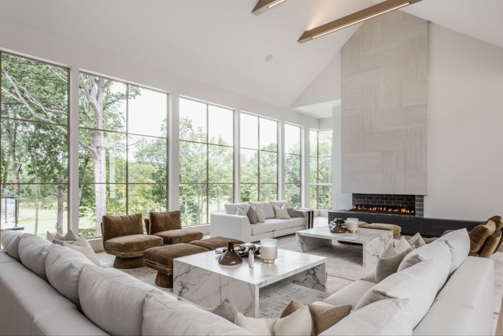 Modern luxury living room at "The Reverie" estate in Zionsville, Indiana, featuring a floor-to-ceiling fireplace, soaring architecture, and marble tables