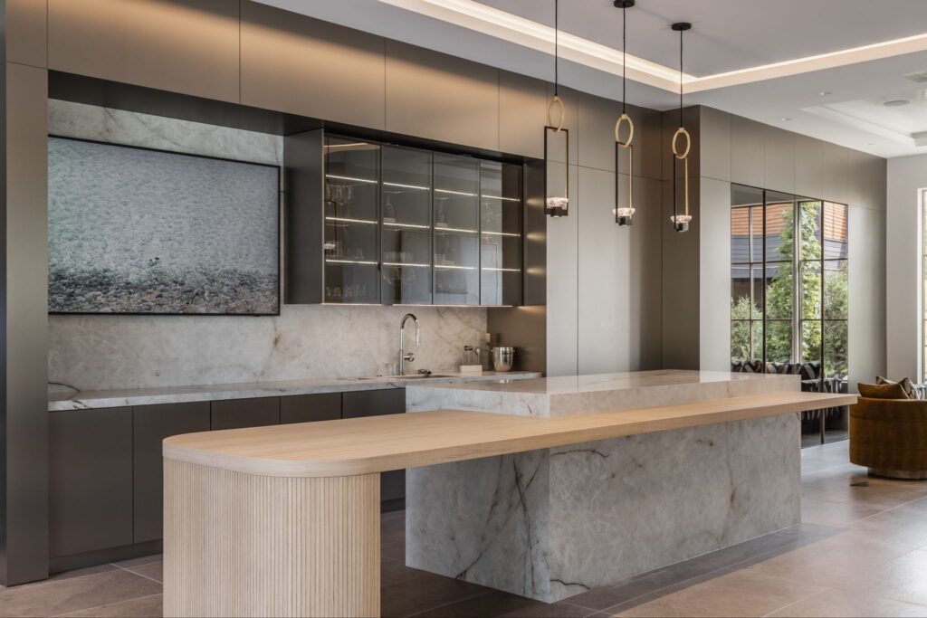 Modern luxury kitchen and wet bar at "The Reverie" estate in Zionsville, Indiana, featuring a marble island, custom Doca cabinetry, and integrated Gaggenau appliances